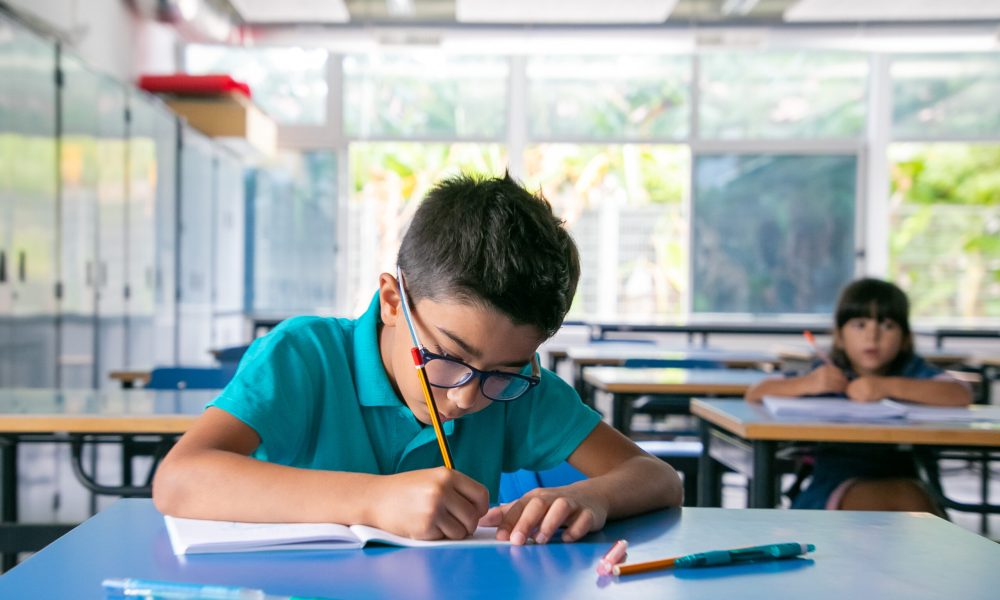 focused young boy in glasses sitting at desk and writing